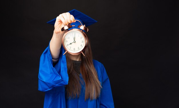 Feche a foto de uma estudante com um manto azul mostrando o despertador