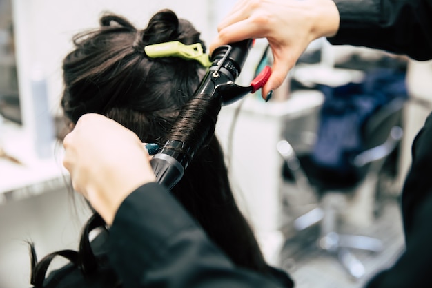 Feche a foto de uma linda mulher com lindos cabelos ondulados, fazendo seu cabelo em um salão de beleza.