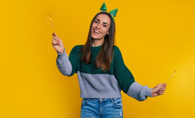 Feche a foto de uma linda mulher feliz e elegante em um suéter casual de natal com estrelinhas nas mãos posando isolado em um fundo amarelo e se divertindo