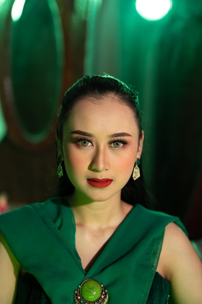 Feche a foto de uma mulher asiática com o rosto cheio de maquiagem e vestindo roupas verdes e joias nas orelhas