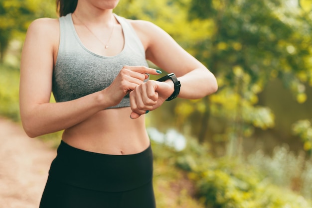 Feche a foto de uma mulher esportiva usando smartwatch ao ar livre no parque durante o pôr do sol