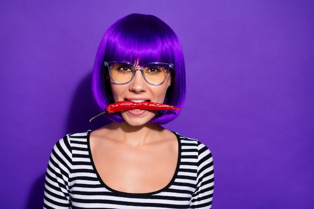 Foto feche a foto de uma senhora encantadora segurando pimenta malagueta, parecendo vestindo uma peruca roxa, camisa listrada isolada com fundo violeta