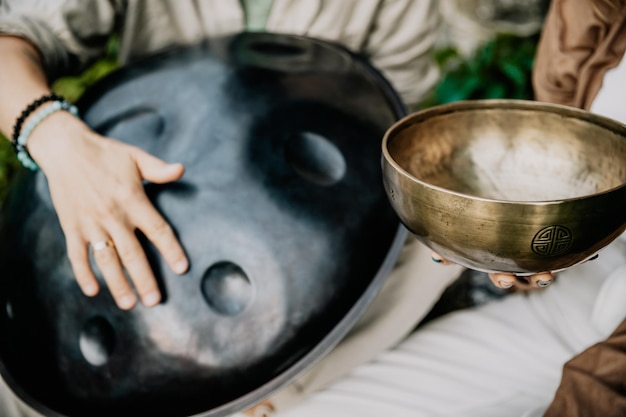 Feche a foto do handpan em um dueto com tigelas tibetanas nas mãos dos mestres