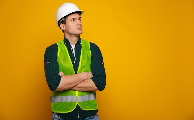 Feche a foto do jovem capataz ou arquiteto feliz e confiante no capacete de construção está posando isolado em fundo amarelo.