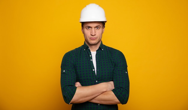 Feche a foto do jovem capataz ou arquiteto feliz e confiante no capacete de construção está posando isolado em fundo amarelo.