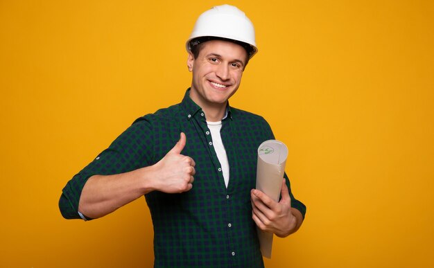 Feche a foto do jovem capataz ou arquiteto feliz e confiante no capacete de construção está posando isolado em fundo amarelo.