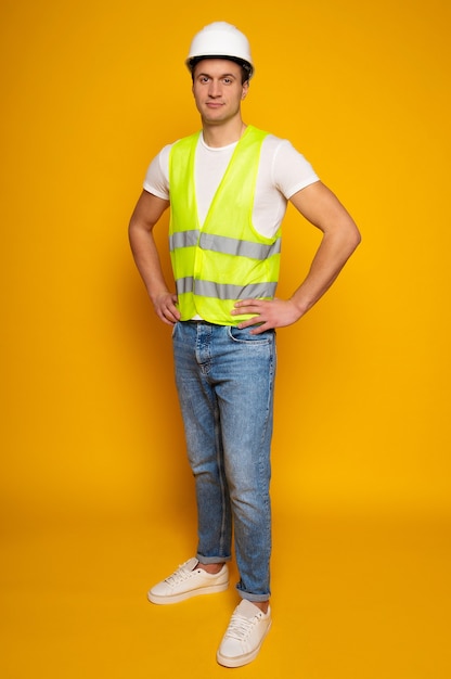 Foto feche a foto do jovem capataz ou arquiteto feliz e confiante no capacete de construção está posando isolado em fundo amarelo.