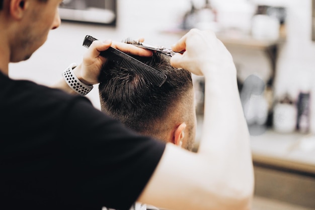 Feche a foto recortada de um cabeleireiro que trabalha para um jovem bonito na barbearia