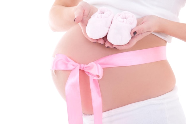 Feche a imagem da barriga da mulher grávida com fita rosa e botinhas de bebê