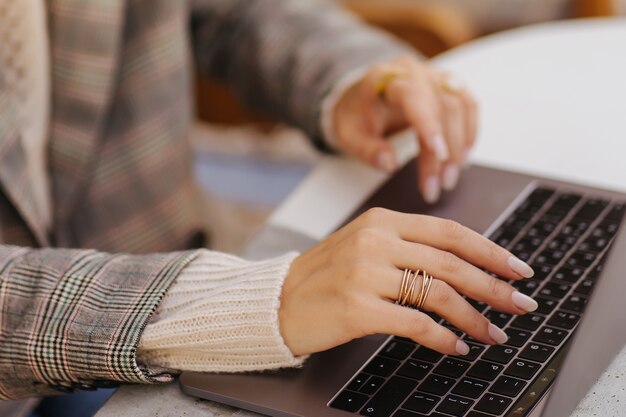Feche a imagem das mãos de mulher digitando e escrevendo no laptop, trabalhando no café.