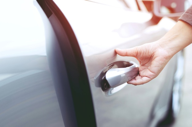 Feche a imagem de um empresário com a mão na alça abrindo a porta de um carro.