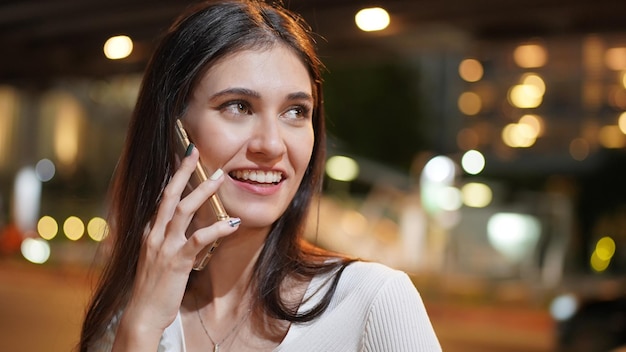 Feche a jovem mulher falando com alguém em seu celular enquanto olha para a distância com expressão facial feliz.