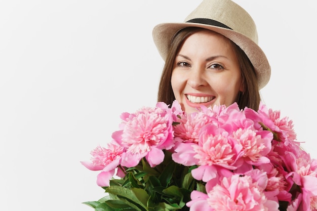 Feche a jovem mulher tenra no vestido azul, chapéu segurando o buquê de flores de peônias rosa isoladas no fundo branco. Dia de São Valentim, conceito de feriado do dia internacional da mulher. Área de publicidade.