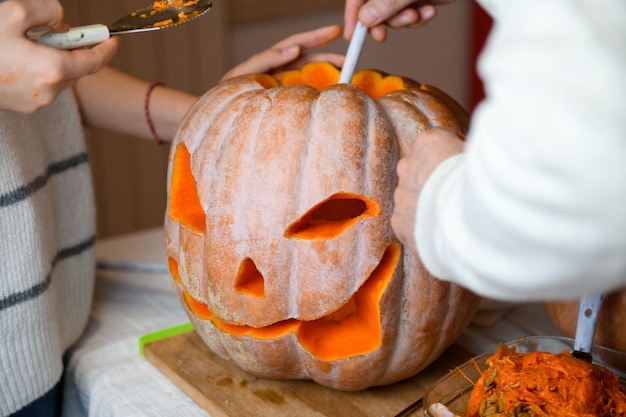 Feche a mão da filha e do pai que puxa sementes e material fibroso de uma abóbora antes de esculpir para o Halloween