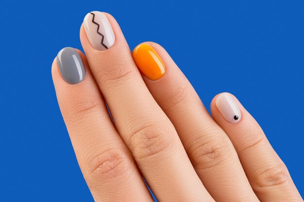 Feche a mão da mulher com uma manicure minimalista moderna em um design de unhas de outono com fundo azul