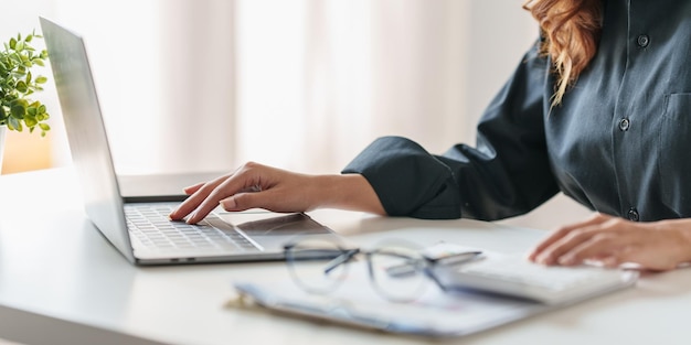 Feche a mão da mulher de negócios usando a calculadora para calcular no laptop os resultados financeiros e o orçamento da empresa Conceito de auditoria de contas