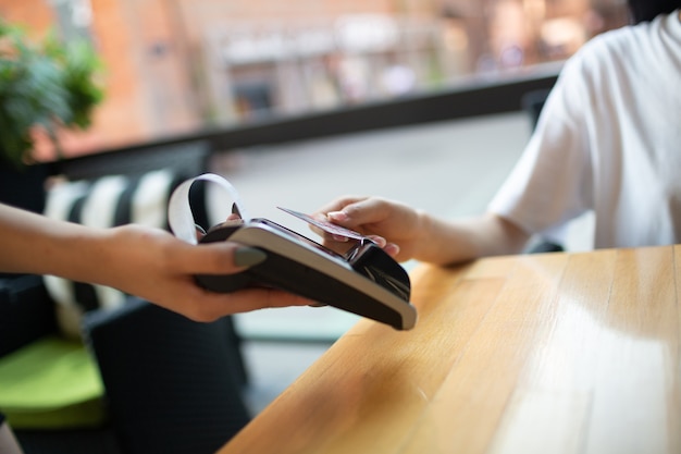 Feche a mão da mulher e pague com o caixa do terminal de pagamento sem contato com cartão de crédito em um café ao ar livre