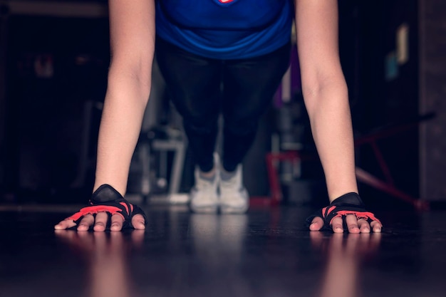 Feche a mão da mulher fazendo exercícios de flexões em uma academia na ginástica de conceito noturno mãos em luvas pretas sem dedos closeup no chão