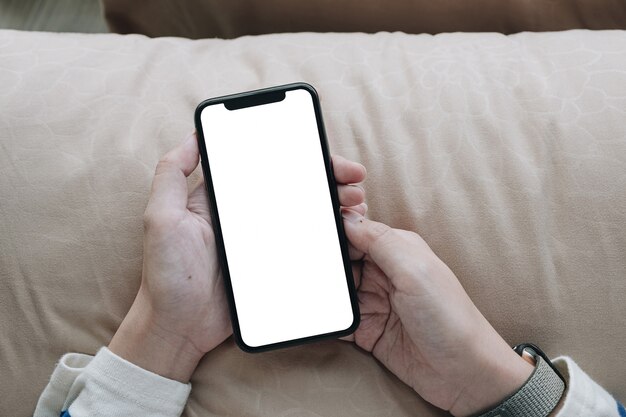 Feche a mão da mulher usando um telefone inteligente com tela em branco em casa.