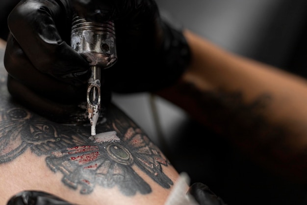 Feche a mão de um tatuador com luva preta e sua máquina de tatuagem Conceito de arte corporal