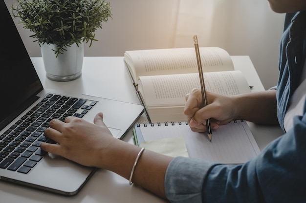 Feche a mão de uma estudante do ensino médio estudando, aprendendo lições acadêmicas on-line na biblioteca da universidade usando o computador portátil, conceito de educação.