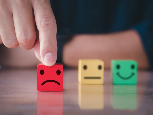 Feche a mão do homem escolha o ícone de rosto sorridente infeliz no cubo de madeira Conceito de pesquisa de satisfação do cliente