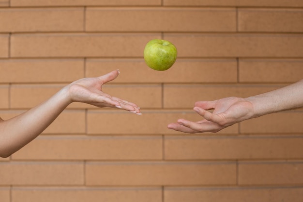 Feche a mão do homem jogando a maçã verde enquanto a palma da mulher a pega