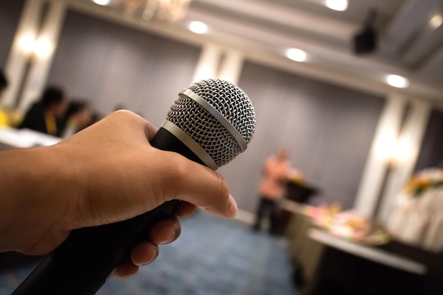 Feche a mão do homem segurando o microfone na sala de conferências ou evento de reunião com fundo desfocado