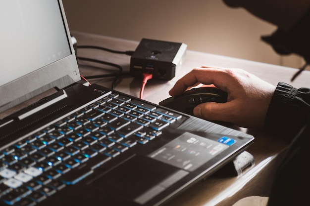 Feche a mão do homem usando mouse sem fio, Raspberry Pi, laptop com teclado retroiluminado azul