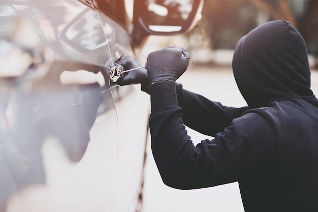 Feche a mão do ladrão de carros segurando a chave de fenda, adulterando o puxão e a luva preta roubando o automóvel tentando a maçaneta da porta para ver se o veículo está destrancado tentando arrombar o interior