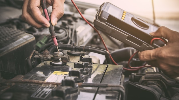 Feche a mão do mecânico de automóveis usando a ferramenta de medição, verificando a bateria do carro.