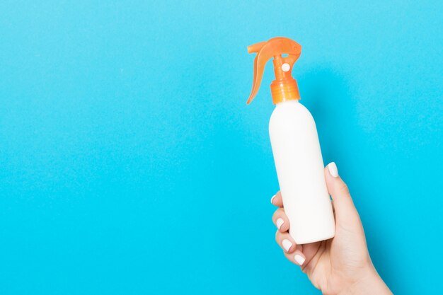 Feche a mão feminina segurando um spray de produtos cosméticos em fundo azul, com espaço de cópia