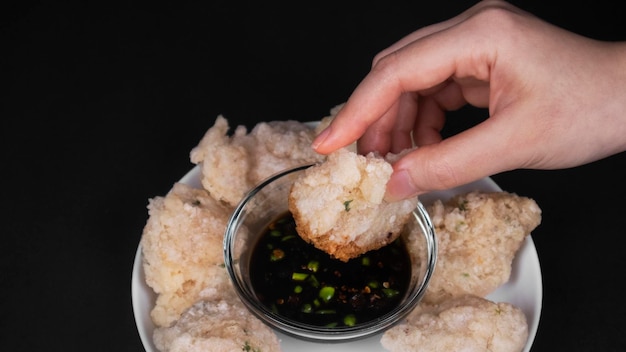 Feche a mão mergulhando uma farinha de tapioca frita em um molho de soja e pimenta