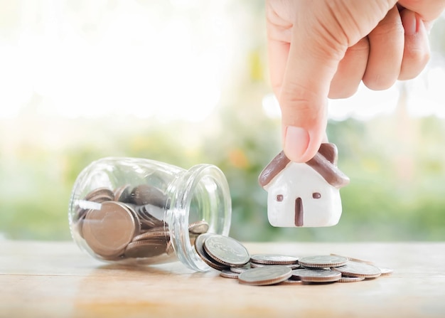 Feche a mão segurando uma casa em miniatura economizando dinheiro para comprar uma casa conceito de propriedade de investimento