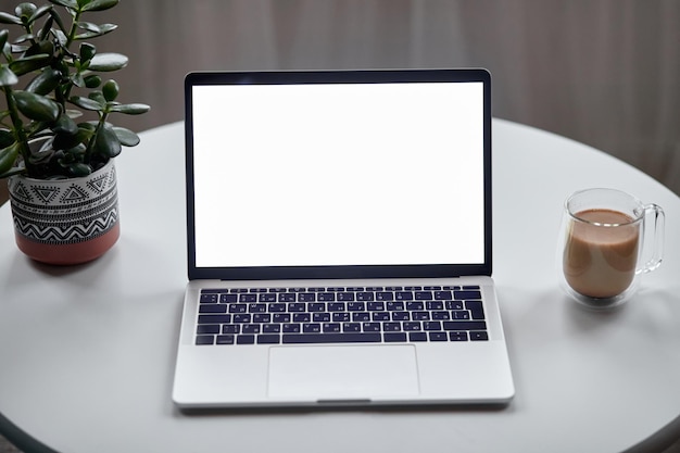 Feche a maquete da tela do laptop na mesa com uma xícara de café e uma planta de casa em casa sem pessoas