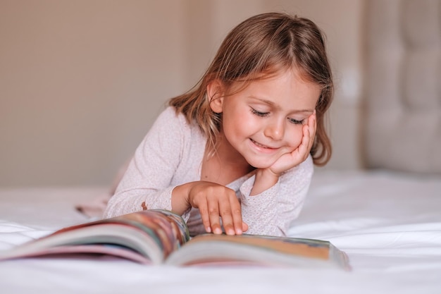 Feche a menina focada na leitura do livro na camaDia internacional da alfabetização