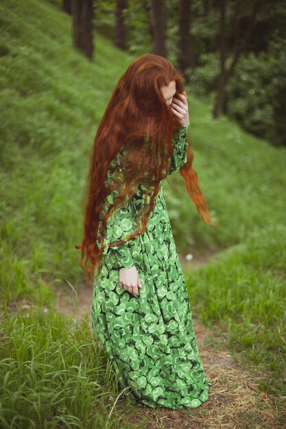 Feche a mulher de cabelos ruivos em um vestido longo parado na foto do retrato do caminho