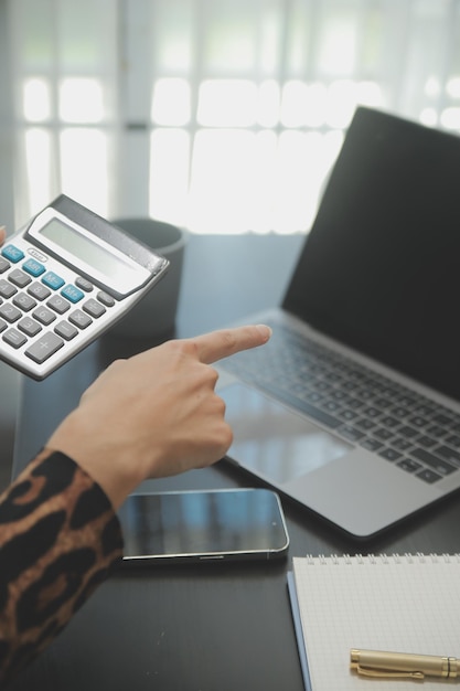 Foto feche a mulher de negócios usando calculadora e laptop para fazer finanças matemáticas em estatísticas de contabilidade fiscal de mesa de madeira e conceito de pesquisa analítica