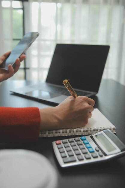 Feche a mulher de negócios usando calculadora e laptop para fazer finanças matemáticas em estatísticas de contabilidade fiscal de mesa de madeira e conceito de pesquisa analítica