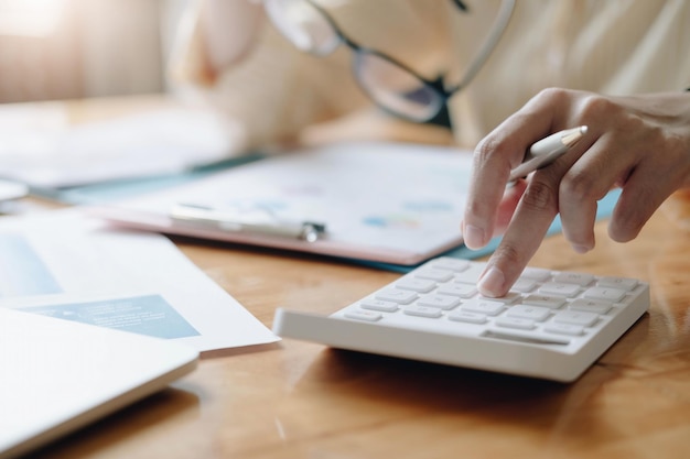 Feche a mulher de negócios usando calculadora e laptop para fazer finanças matemáticas na mesa de madeira no escritório e fundo de trabalho de negócios, impostos, contabilidade, estatística e conceito de pesquisa analítica