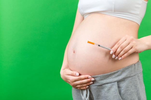 Feche a mulher grávida segurando a seringa de insulina contra a barriga no fundo colorido com espaço de cópia Conceito de diabetes