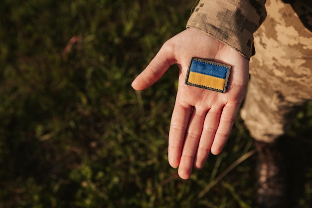 Feche a mulher militar segurando o remendo de velcro com a bandeira da Ucrânia