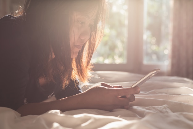 Feche a mulher usando o smartphone na cama. Foco no rosto