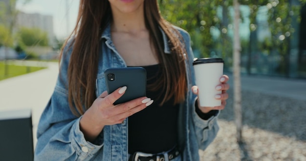 Feche a mulher usando smartphone na rua Mulher bonita usando telefone com café para viagem na rua Comunicação conceito de rede social de bate-papo de compras on-line