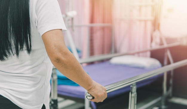 Feche a paciente mais velha andando em barras paralelas na sala de reabilitação ao fundo no hospital