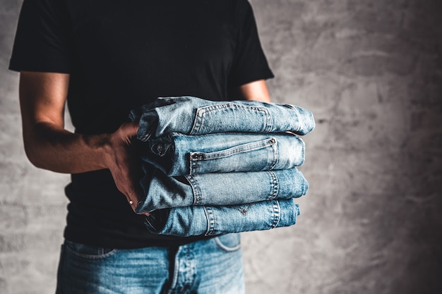 Feche a pilha de jeans azul dobrado na mão sobre a parede cinza