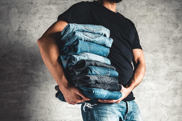 Feche a pilha de jeans azul dobrado na mão sobre o fundo da parede cinza, copie o espaço