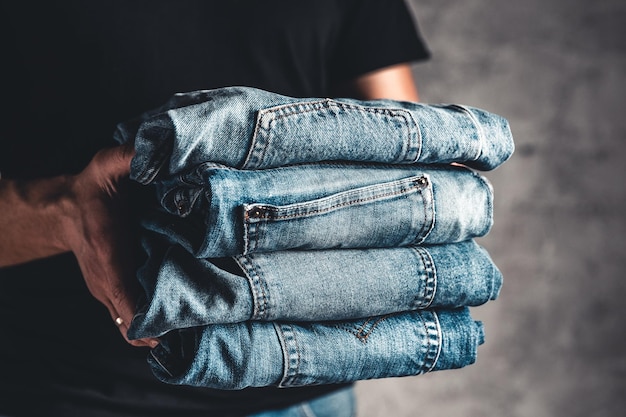 Foto feche a pilha de jeans azul dobrado na mão sobre o fundo da parede cinza, copie o espaço