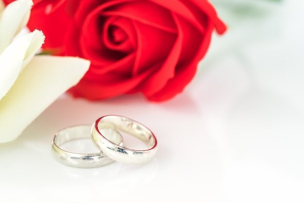 Feche a rosa vermelha e a aliança de casamento em fundo branco, conceito de casamento com rosas e anel