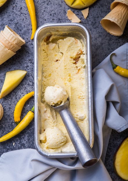 Foto feche a tigela com sorvete de baunilha, coberto com pimenta malagueta e frutas frescas de manga na superfície escura.